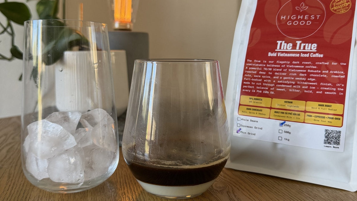 Phin-brewed coffee layered over sweetened condensed milk next to a glass of ice and a bag of Highest Good The True