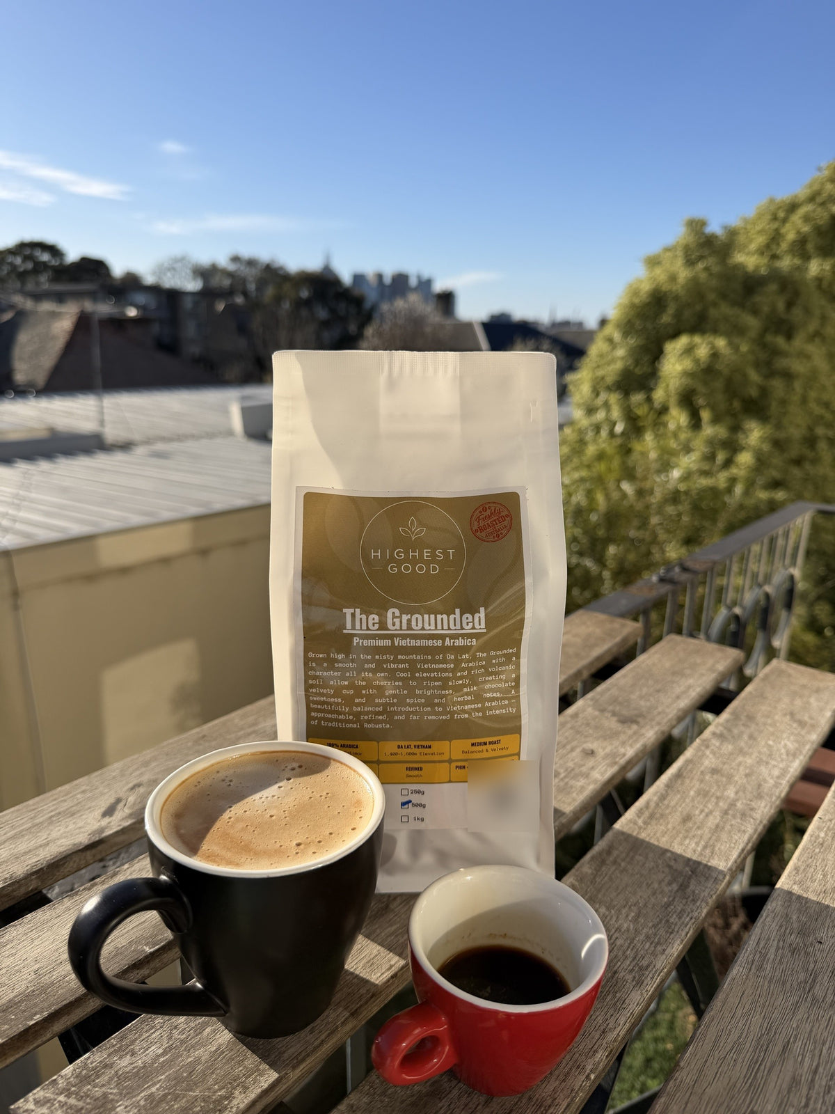 Highest Good The Grounded Vietnamese Arabica coffee beans with a latte and espresso on a sunny balcony
